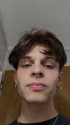 a young man with piercings on his nose looks at the camera while standing in front of a door