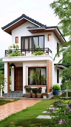 a white house with brown trim and plants in the front yard, surrounded by greenery