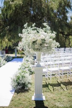 an outdoor ceremony setup with white chairs and flowers on the back of each chair,