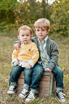 two young boys sitting on top of a wooden crate in the grass with their arms around each other