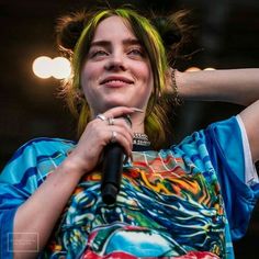 a woman holding a microphone in her right hand and looking up at the sky with lights behind her