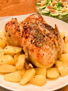 a white plate topped with chicken and potatoes next to a salad on a wooden table