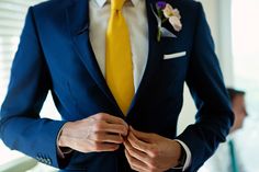 a man in a blue suit with a yellow tie and flower boutonniere