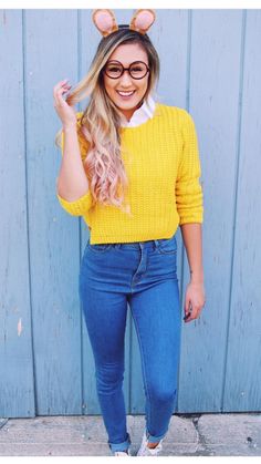 a woman wearing glasses and a yellow sweater is standing in front of a blue wall