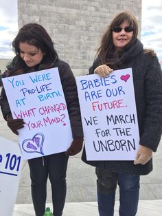 two women holding signs that say babies are our future and we march for the unicorn