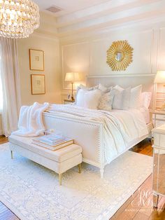 a white bed sitting in a bedroom next to a chandelier above a window