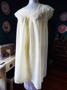 A winsome yellow nightgown from the 1960s by the brand Shadowline. The material is most likely a cotton-synthetic blend. The gown has an adorable short cut with cap sleeves that feature delicate flowers in yellow and white on a sage green vine. The gown is in great condition.  Length approx 35.5", bust armpit to armpit 21.25". I estimate this is a modern women's M, or about a size 8-10. I recommend to carefully check your own measurements before purchase.  Mannequin measurements are: Bust 35.5/W Vintage Cotton Nightgown For Summer, Spring Vintage Cotton Nightgown, Vintage Cotton Nightgown For Spring, Vintage Cotton Home Dress, Vintage Cotton Sleepwear For Summer, Retro Summer Nightgown For Sleep, Yellow Cotton Short Sleeve Sleepwear, Retro Lace Trim Nightgown For Sleep, Vintage Short Sleeve Nightgown