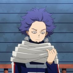 a man with purple hair sitting in front of a stack of papers and looking at the camera