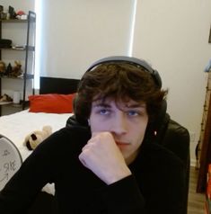 a young man sitting in front of a bed wearing headphones and looking at the camera