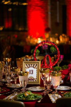 the table is set with plates, silverware and wine glasses in front of a clock