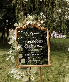 a sign that is in the grass with flowers on it and greenery around it