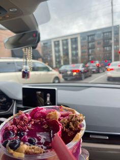 an ice cream sundae with blueberries and crumbles in a cup on the dashboard of a car