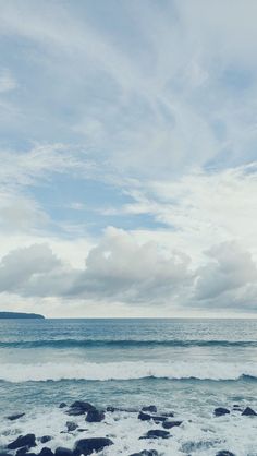 an ocean view with waves crashing on the shore and clouds in the sky above it