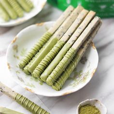 some green sticks are on a white plate and next to two bowls filled with powder