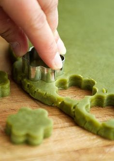 a person is making green cookies on a cutting board