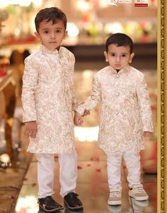 two young boys dressed in white outfits holding hands and standing next to each other on a tiled floor