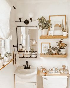 a white bathroom with plants and pictures on the wall above the toilet, along with a sink