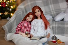 two dolls are sitting on a blanket next to a christmas tree