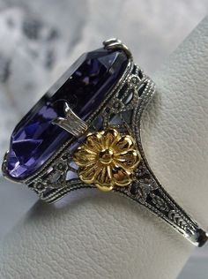 Simulated Amethyst Sterling Silver Ring Gold Daisy#D208 This is a brand-new Vintage revival sterling silver filigree ring. This is a flawless man-made purple amethyst, 18mm by 13mm in size. The ring is 3/4" (19mm) North to South on the finger. Notice the intricate and detailed floral design of the antique patina silver filigree that travels all the way down the band, with a delicate rose gold flower on each side. The inside of the band is marked 925 for sterling silver. This ring has style and c Amethyst Art, Daisy Vintage, Ring Rectangle, Rose Gold Flower, Art Deco Floral, Vintage Revival, Purple Amethyst Ring, Deco Floral, Sterling Silver Filigree