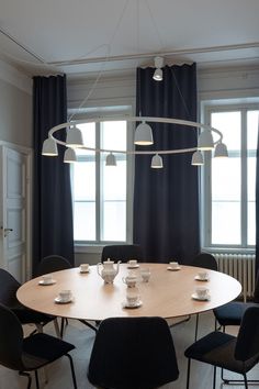 a round table with black chairs and white plates on it in front of two windows