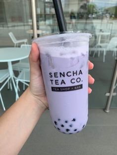 a person holding up a purple drink in front of a glass window with the words senda tea co on it