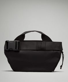 a black bag with a belt on the front and shoulder strap, sitting against a gray background