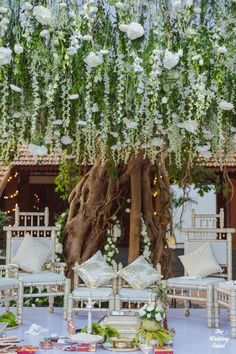 an outdoor seating area with white flowers and greenery hanging from the ceiling above it