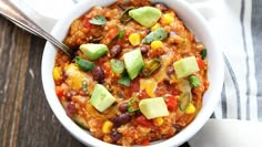 a white bowl filled with chili, corn and avocado on top of a wooden table