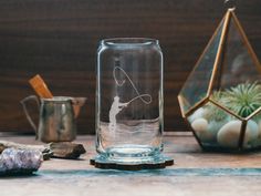 a glass vase with a fishing scene etched on the inside sits next to some rocks and airplants