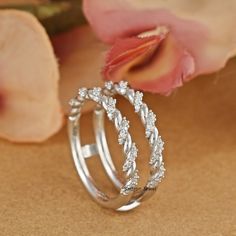 two wedding rings with diamonds on top of each other next to a flower and petals