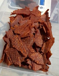 a plastic container filled with pieces of bacon on top of a counter next to an electronic device