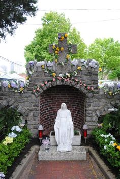 a statue in the middle of a garden with flowers around it and a cross on top