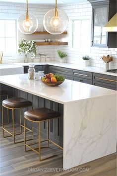 a kitchen island with marble counter tops and stools in front of two hanging lights