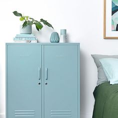 a blue locker next to a bed in a room with a plant on top of it