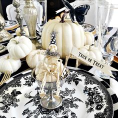 a table set for halloween with white pumpkins, black and white plates and silverware