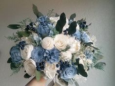 a bouquet of blue and white flowers in someone's hand on a wall background