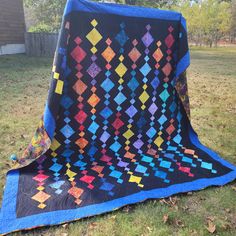 a quilted blanket sitting on top of a grass covered field