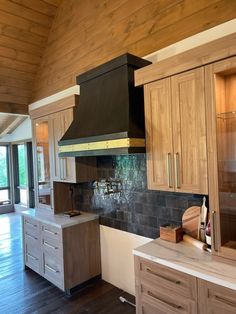 a large kitchen with wooden cabinets and black range hood over the island in front of an open floor plan