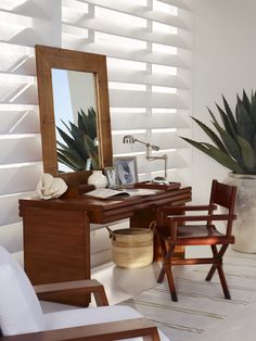 a desk with a mirror, chair and potted plant on it in a white room