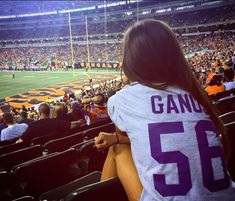 a woman is sitting in the stands at a football game with her back to the camera