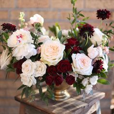 a vase filled with white and red flowers sitting on top of a wooden table next to a brick wall