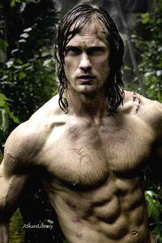 a shirtless man standing in front of some trees and bushes with his hands on his hips