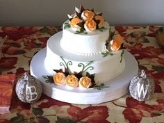 a three tiered wedding cake with orange flowers on top and two silver ornaments around it