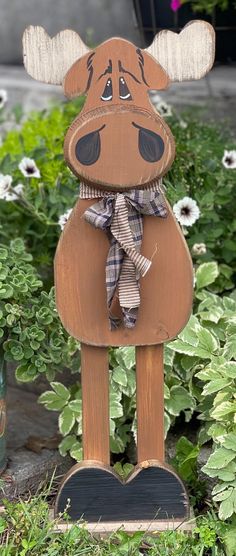 a wooden moose with a plaid bow on it's head standing in the grass