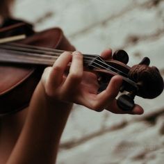 a close up of a person holding a violin and playing it with both hands,