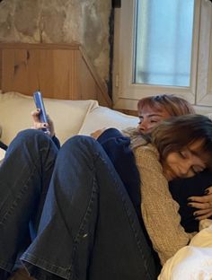 two women sitting on a bed with their arms around each other and one holding a cell phone