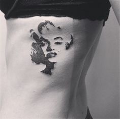 a woman's stomach with black and white tattoos on her side, showing the face of marilyn monroe