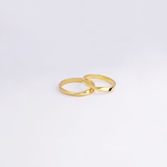 two gold wedding rings sitting on top of a white surface with one ring facing the other way