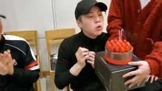 two men sitting at a table and one is holding a cake with candles in it