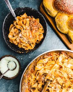 two pans filled with pasta next to buns and bread on a table top